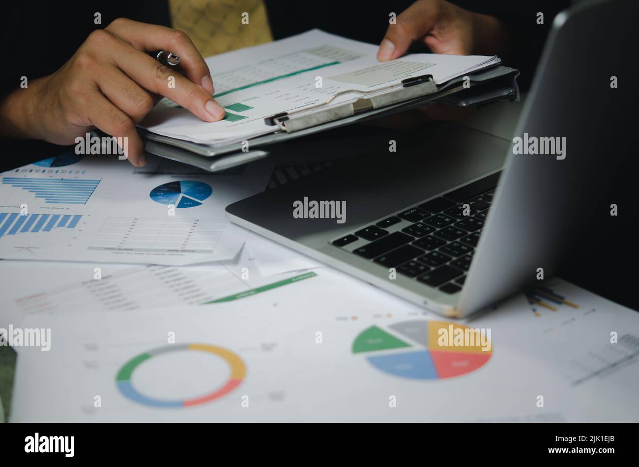 Uomo d'affari persona che punta documento grafico di marketing finanziario rapporto e carta di lavoro grafico di analisi investimento con computer portatile sulla scrivania in ufficio. Foto Stock