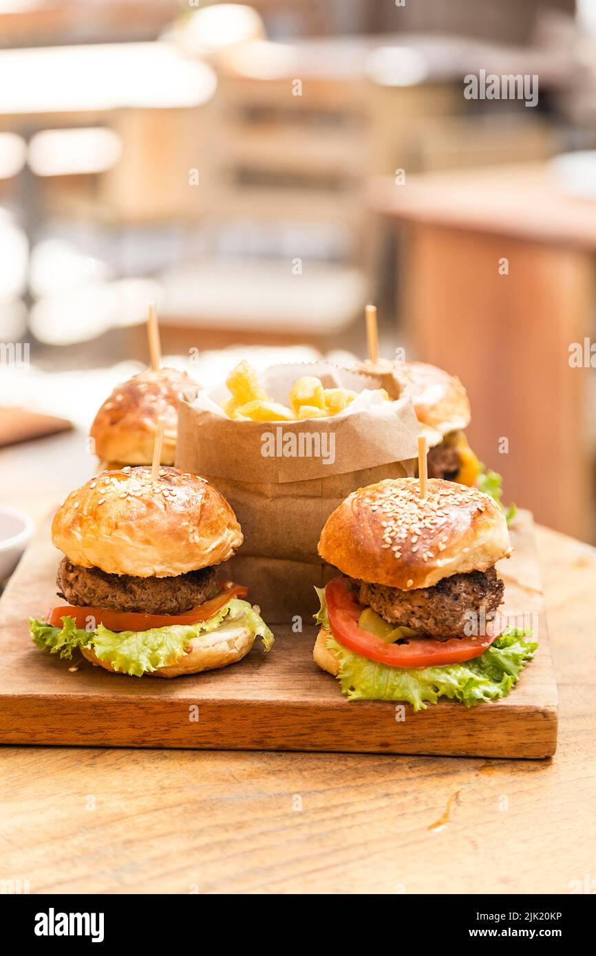 Quattro hamburger su un asse di legno e patatine fritte servite in un cestino di carta di legno in un ristorante Foto Stock