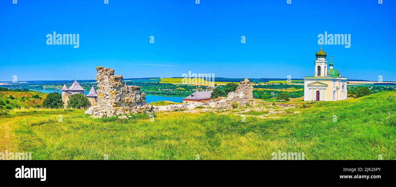 Panorama del prato verde con alte erbe, rovine medievali, chiesa e la storica fortezza di Khotyn, Ucraina Foto Stock