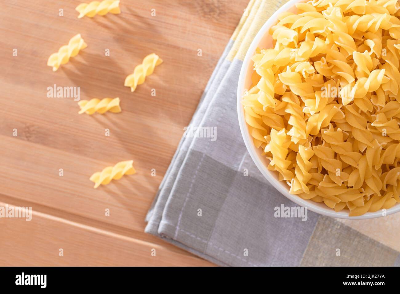 Pasta di Fusilli non cotta in ciotola bianca su tavola di legno. Macaroni crudi e secchi. Cibo malsano e grasso. Cultura Italiana Foto Stock