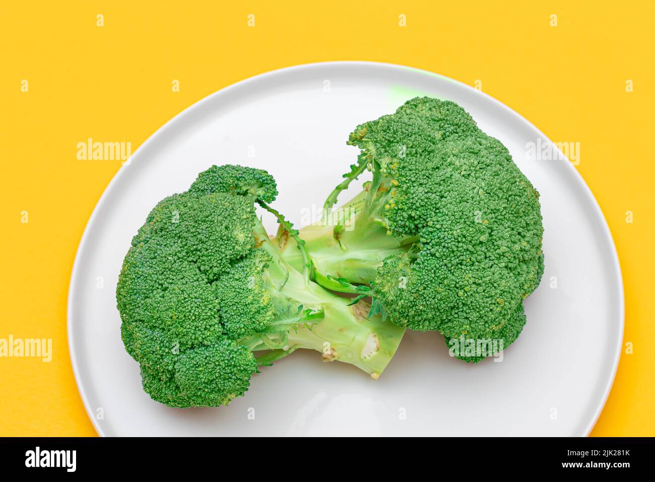 Due pezzi freschi e grezzi di broccoli su piastra bianca. Cavolo verde non fatto. Cultura vegana e vegetariana. Cibo crudo. Alimentazione sana e dieta vegetale Foto Stock