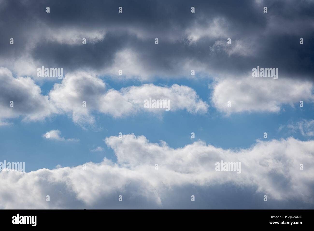 un cielo estivo blu nuvoloso con una banda di nuvole scure sopra e nuvole chiare sotto Foto Stock