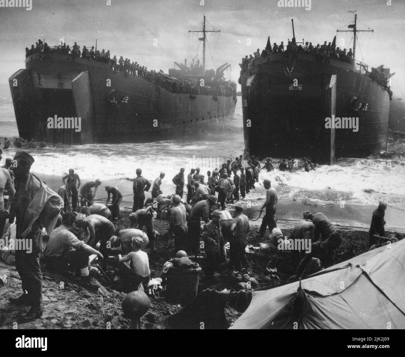 Le due LST, presidiate dalla Guardia Costiera, aprono le loro grandi mascelle nel surf che si lava sulla spiaggia di Leyte Island, mentre i soldati si spogliano e costruiscono dei sandbag che si perforano sulle rampe per velocizzare le operazioni di scarico. Foto Stock