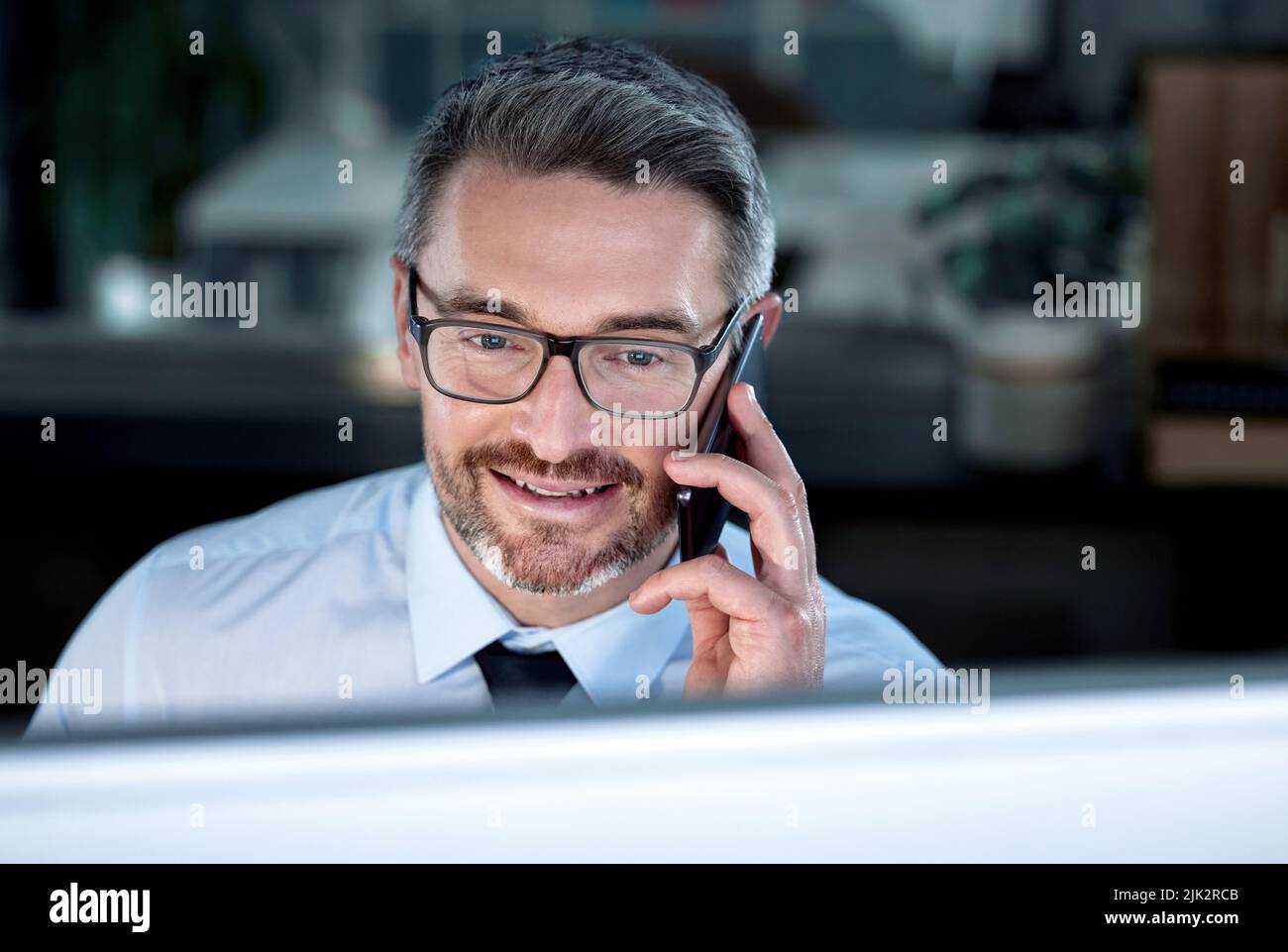 Stavo solo guardandolo, un uomo d'affari che parlava sul cellulare mentre era seduto alla sua scrivania. Foto Stock