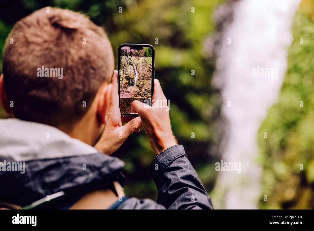 Uomo che fotografa la cascata panoramica con il suo telefono, vista ravvicinata Foto Stock