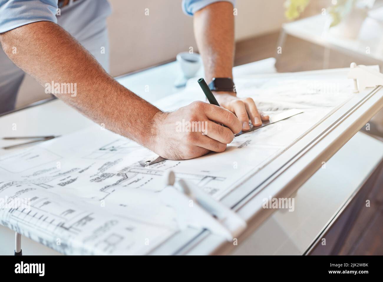 L'architetto maschio ha a disposizione un progetto di costruzione o un piano di costruzione su un tavolo da ufficio. Primo piano dell'uomo caucasico prendendo note di misurazione, schizzi Foto Stock