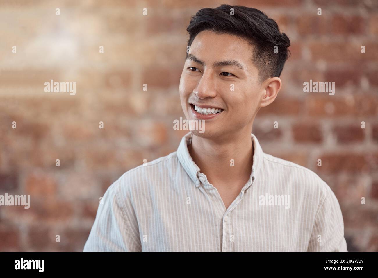 Un uomo d'affari felice, sicuro e sorridente che guarda premuroso mentre lavora in un'agenzia creativa di startup. Designer allegro, affascinante e positivo Foto Stock