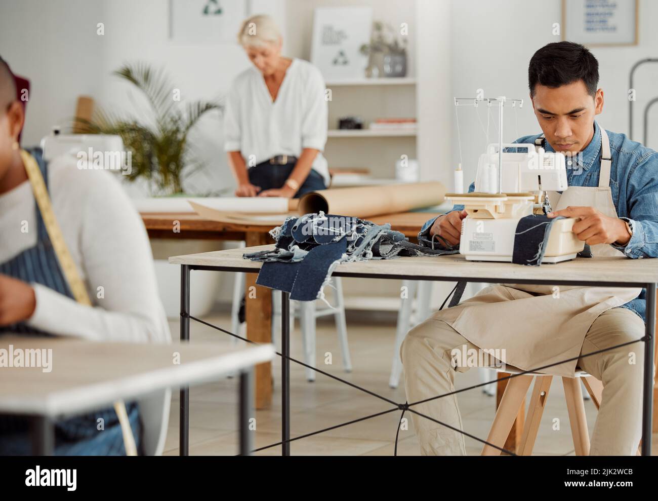 Stilista di moda, giovane uomo e studente creativo in un laboratorio per cucire i vestiti. Operaio di fabbrica, su misura e apprendista imparando le abilità della macchina da cucire Foto Stock