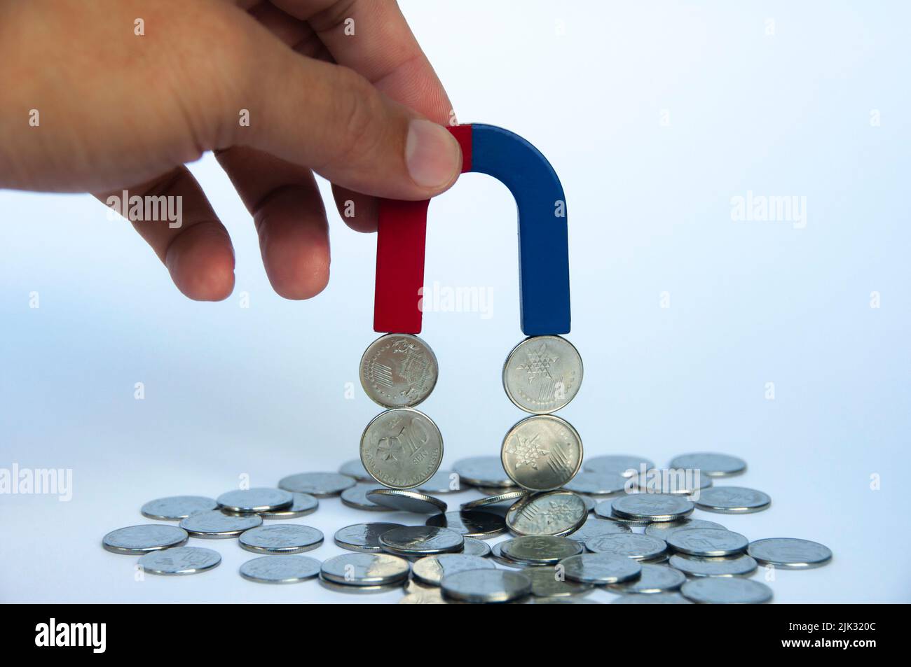 Magnete di tenuta a mano che attrae monete d'argento con fondo di copertura bianco. Concetto di business e legge dell'attrazione Foto Stock