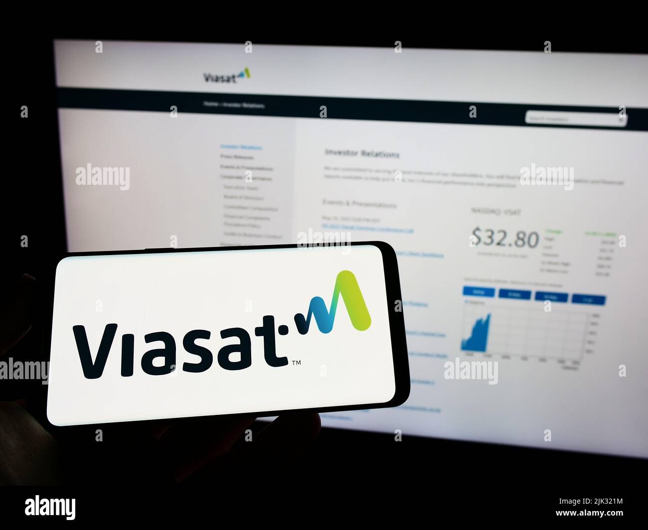 Persona che detiene il telefono cellulare con il logo della società di comunicazione americana Viasat Inc. Sullo schermo di fronte alla pagina web. Mettere a fuoco sul display del telefono. Foto Stock