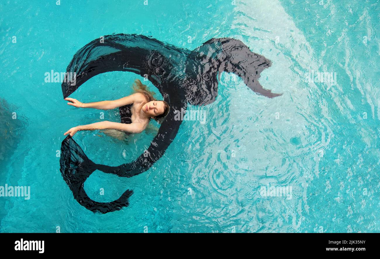Vista dall'alto di bella giovane sexy donna dai capelli scuri galleggiante senza peso elegante in sogno erotico acqua turchese della piscina, il panno si muove dentro Foto Stock