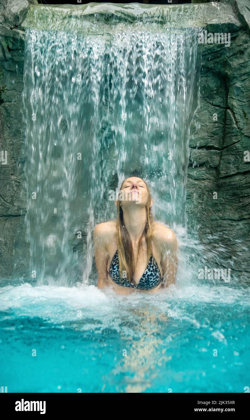Bella donna gode meditativo lo spruzzi d'acqua sotto una cascata nella piscina Spa Wellness, chiude gli occhi sotto l'acqua increspata, spazio copia Foto Stock