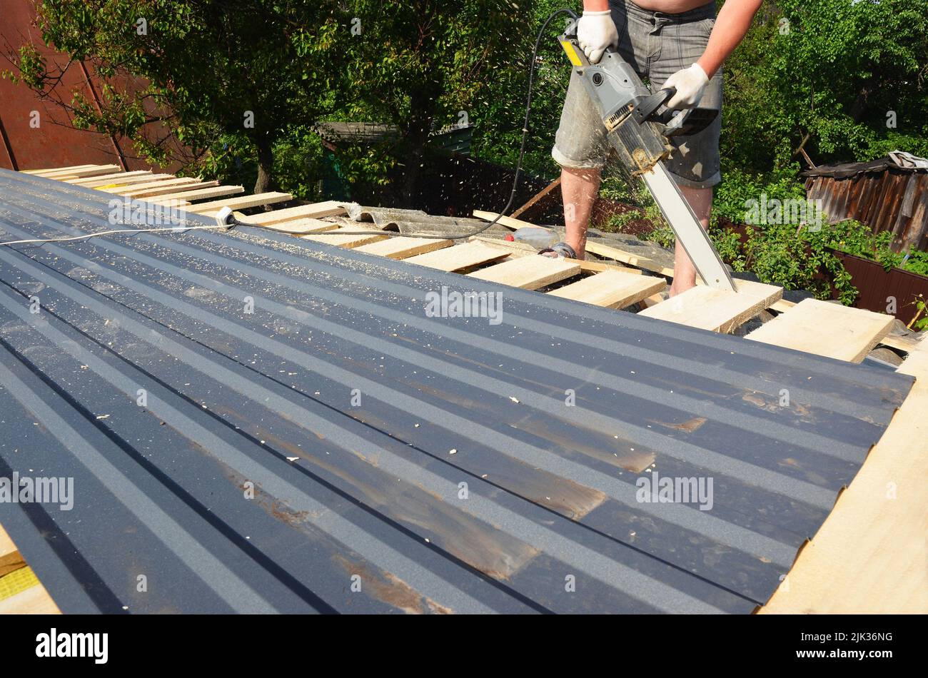 Costruzione di copertura: Un tetto sta tagliando con una sega elettrica pannelli di rivestimento del tetto che fanno il bordo del tetto anche prima di un montaggio di tegole di metallo leggero Foto Stock