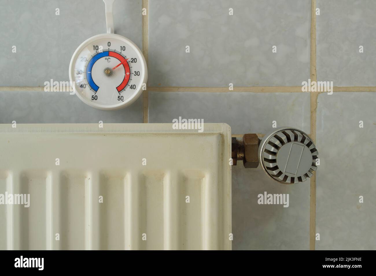 Radiatore, valvola e termometro che mostrano la temperatura profonda nella camera vivente, la mancanza di gas di riscaldamento a causa dell'embargo del petrolio e del gas russi in europa Foto Stock