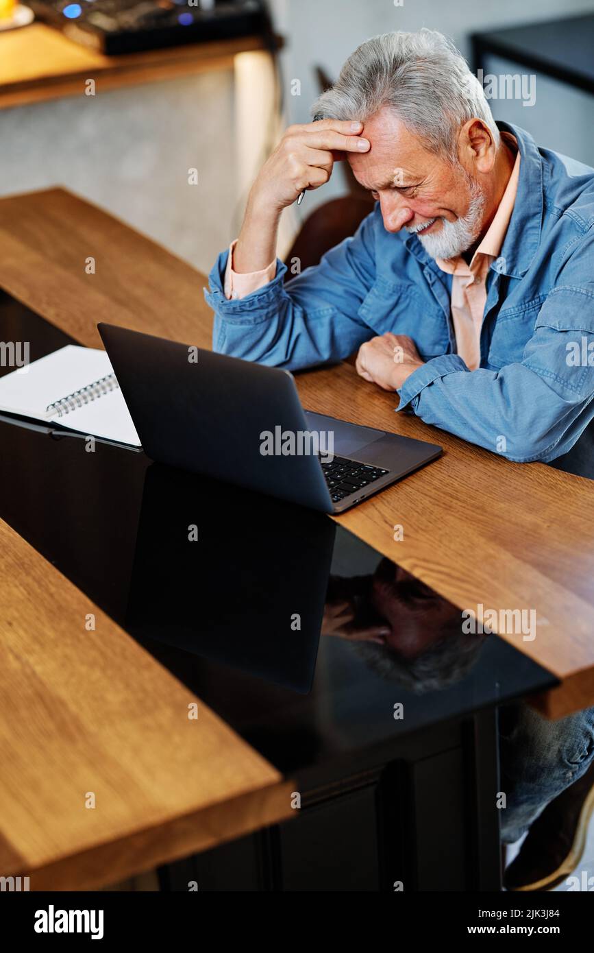 Uno studente anziano seduto in un bar e che ha difficoltà a padroneggiare la lezione sul suo computer portatile. Uno studente anziano che studia nel bar e tiene la sua h Foto Stock