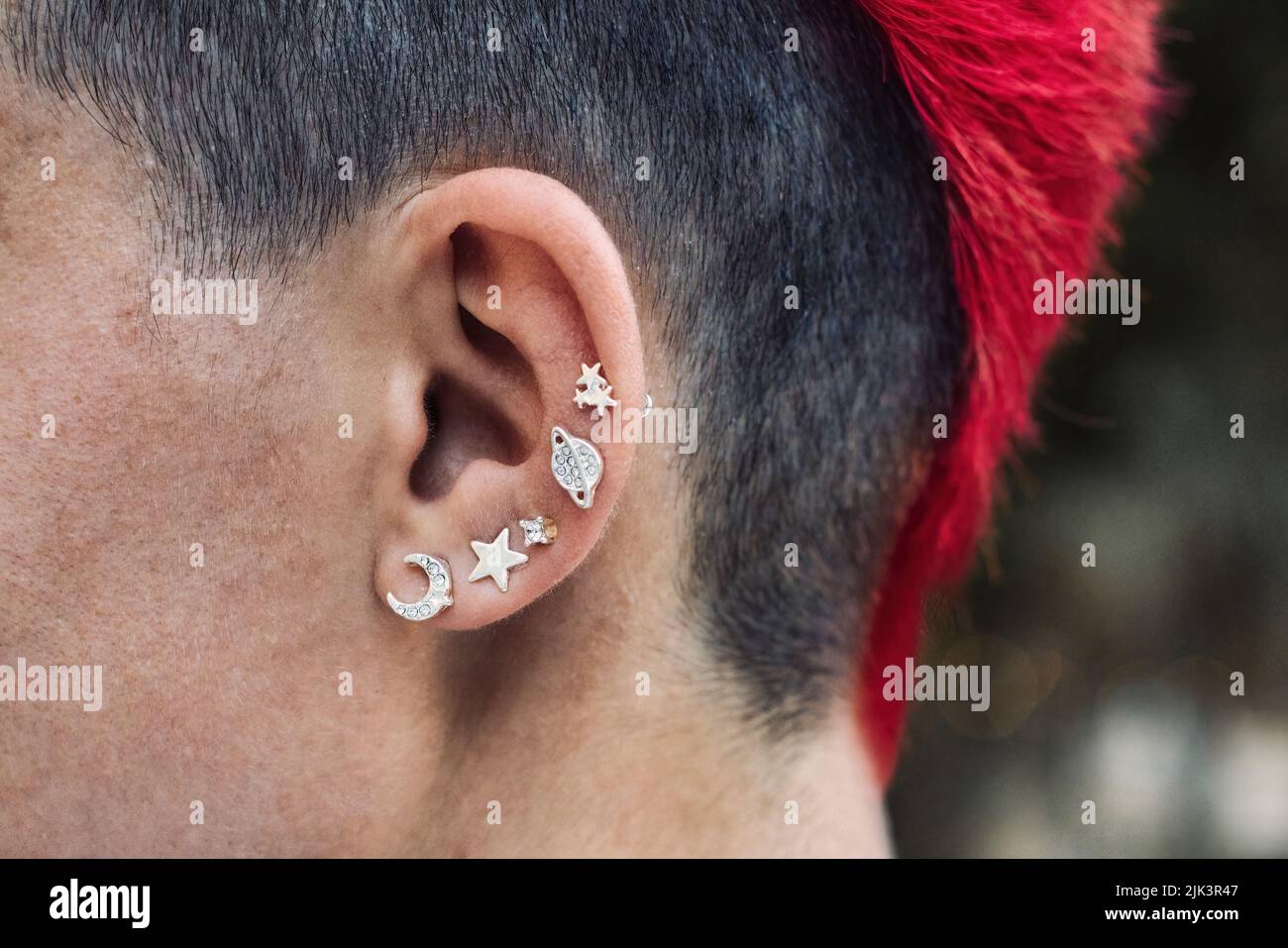 Primo piano dell'orecchio di una punk femminile con piercing in argento e uno stile personale mohawk dai colori rosso brillante Foto Stock