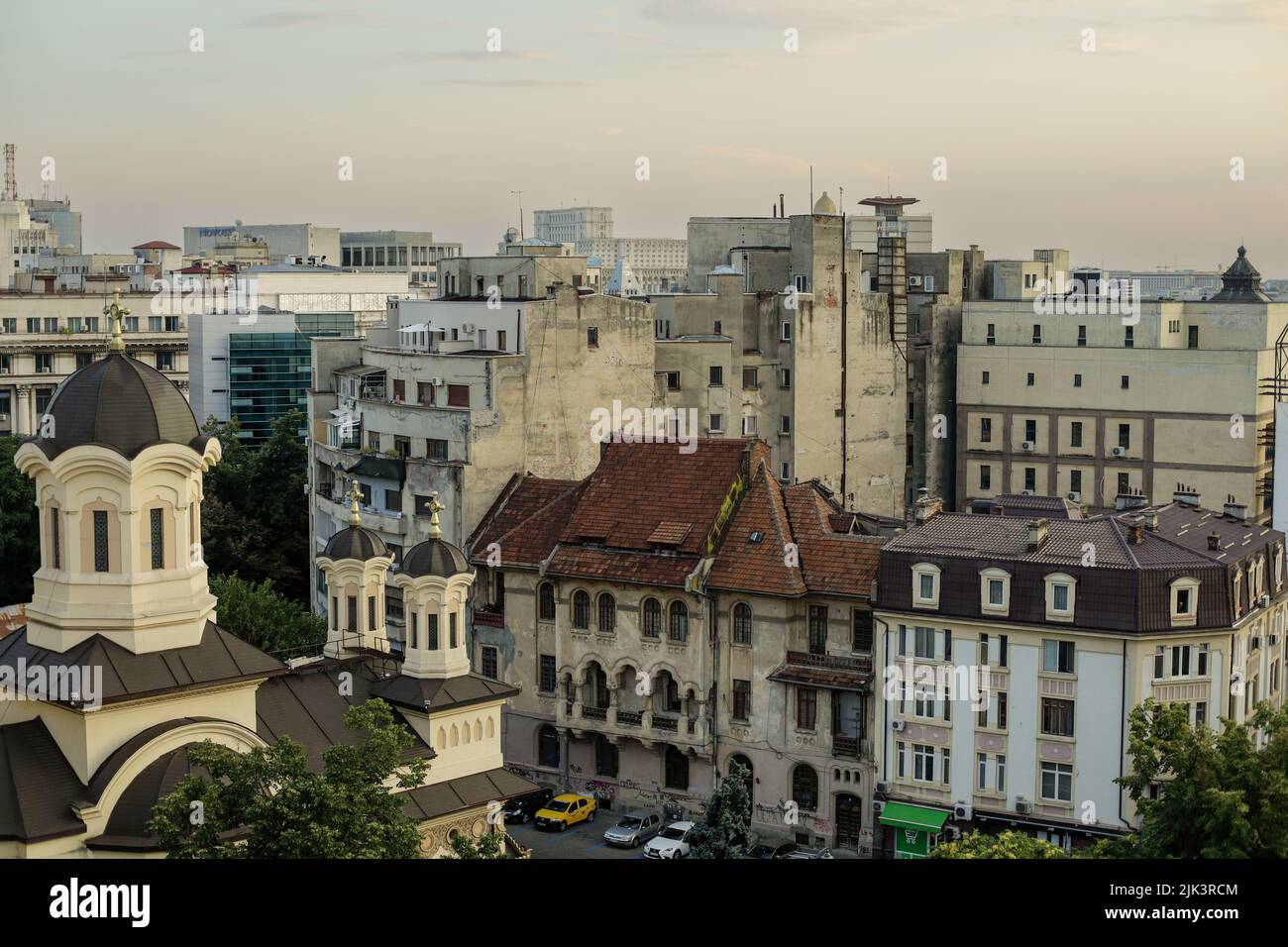 Bucarest, Romania - 30 luglio 2022: Vecchia parte di Bucarest durante un tramonto estivo con edifici nuovi e vecchi insieme e il Palazzo del Parlamento in t Foto Stock