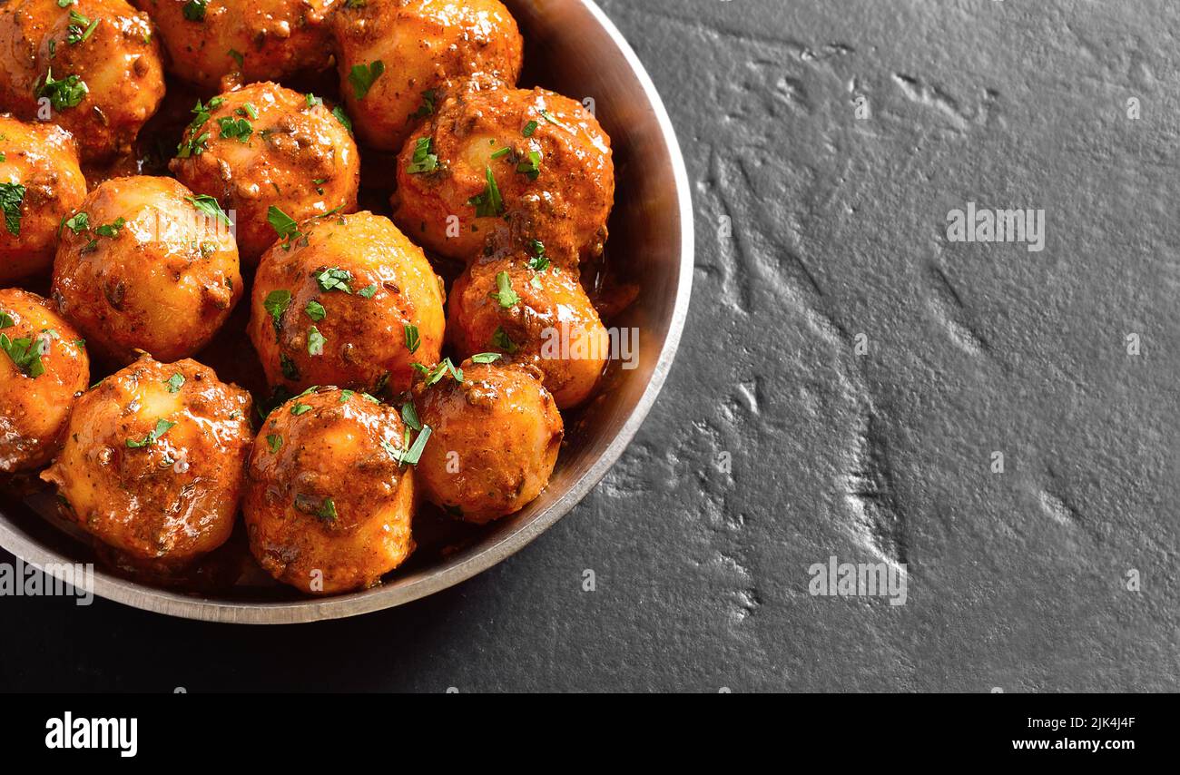 Vista ravvicinata delle piccole patate fritte in padella nel recipiente su sfondo scuro con spazio libero per il testo. Popolare piatto indiano. Foto Stock