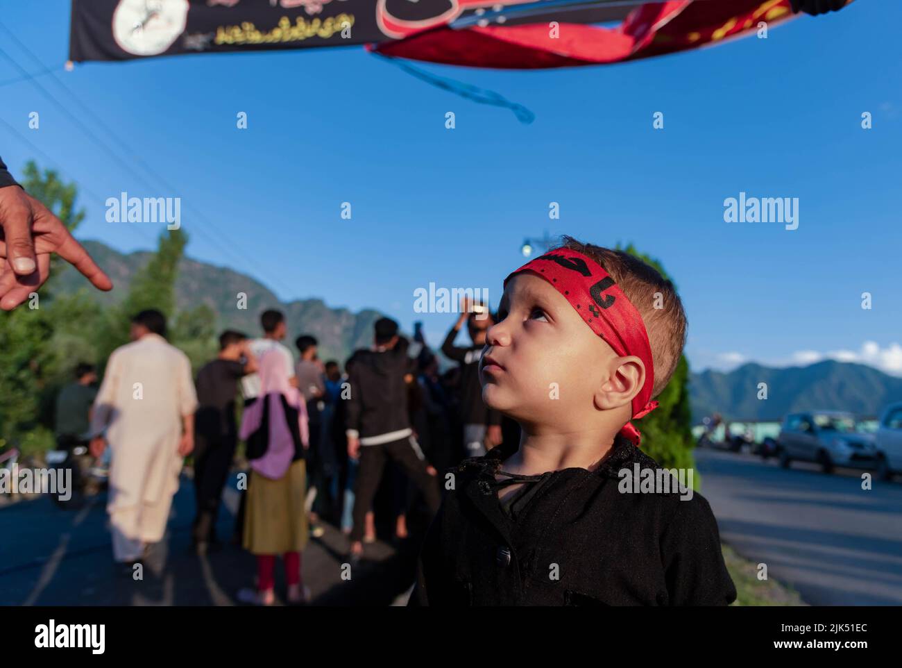 Srinagar. 30 luglio 2022, Srinagar, Jammu e Kashmir, India: Un ragazzo musulmano Kashmiri Shia che indossa un archetto con iscrizioni islamiche guarda verso gli uomini musulmani sciiti che sollevano bandiere e striscioni religiose quando inizia Muharram. Muharram è il primo mese dell'Islam. È uno dei mesi più sacri del calendario islamico. I musulmani sciiti commemorano Muharram come un mese di lutto in ricordo del martirio del nipote del profeta islamico Imam Hussain, nipote di Muhammad, ucciso ad Ashura (10th giorni di Muharram) nella battaglia di Karbala nel 680 d.C. Credit: ZUMA Press, Inc./Alamy Live News Foto Stock