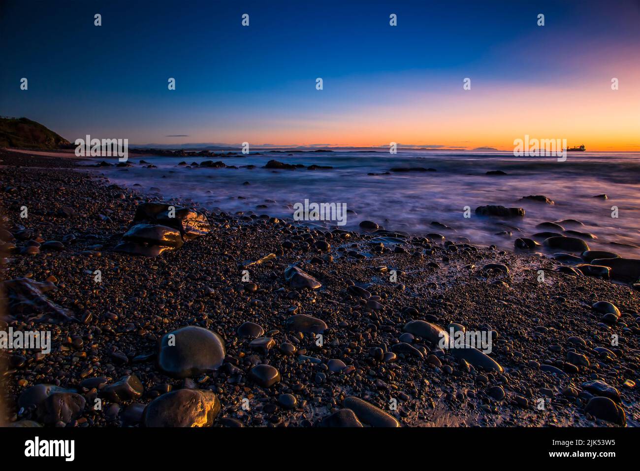 Rocce bagnate ciottoli sulla spiaggia di ciottoli nella cittadina australiana di Forster sulla costa del Pacifico all'alba. Foto Stock