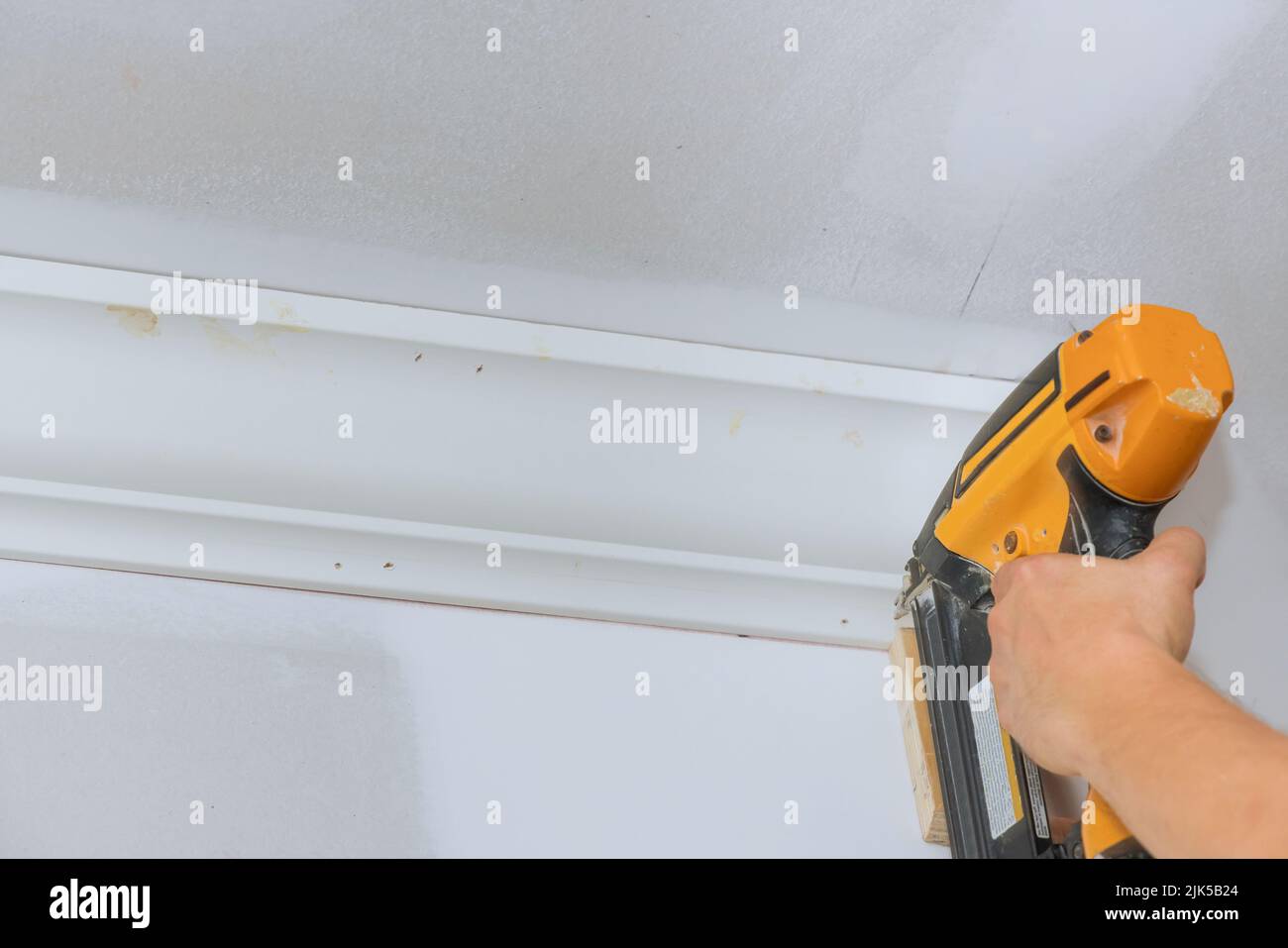 Installazione del soffitto angolo corona stampaggio con l'aiuto di un chiodo pistola ad aria da un falegname Foto Stock