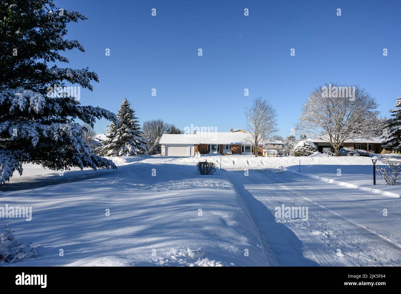 il vialetto coperto di neve conduce fuori e al bungalow coperto di neve dall'altra parte della strada. Foto Stock
