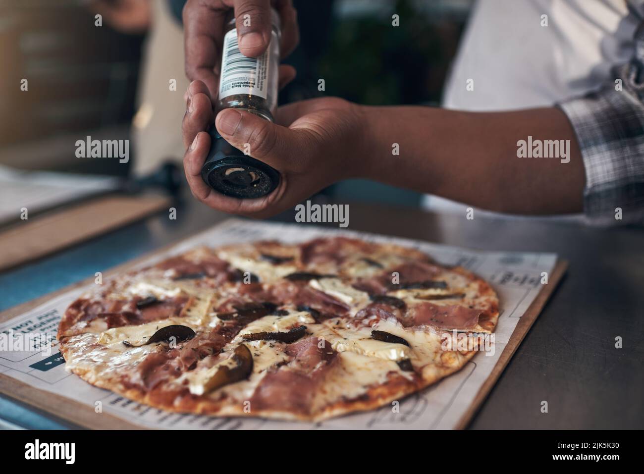 Un po' di condimento va molto lontano: Un uomo irriconoscibile che si alza e prepara una pizza appena fatta da asporto nel suo ristorante. Foto Stock