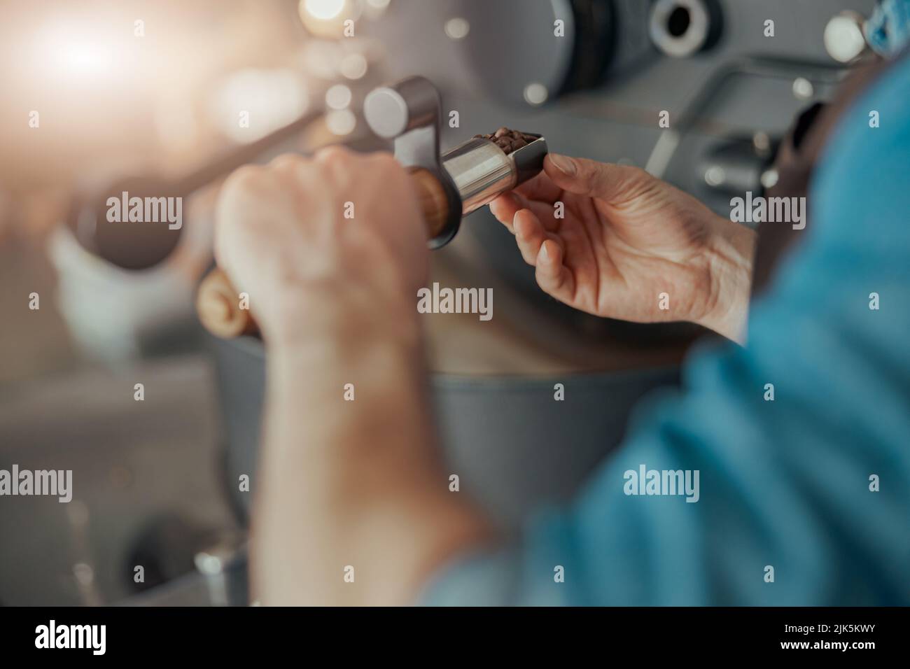 L'uomo tiene i chicchi di caffè appena tostati sullo sfondo della macchina tostatrice Foto Stock