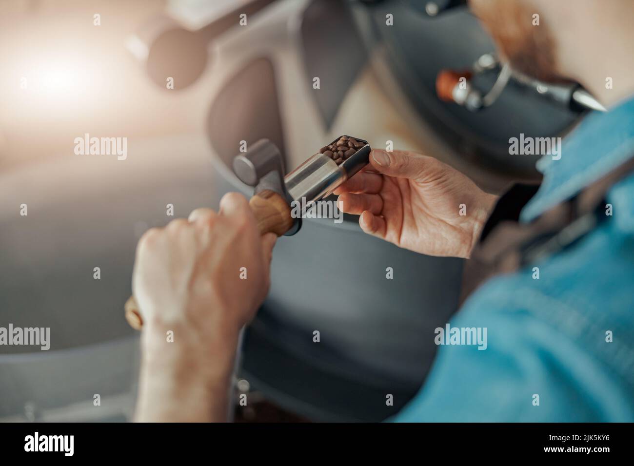 Il barista uomo tiene i chicchi di caffè appena torrefatti sullo sfondo della tostatrice Foto Stock