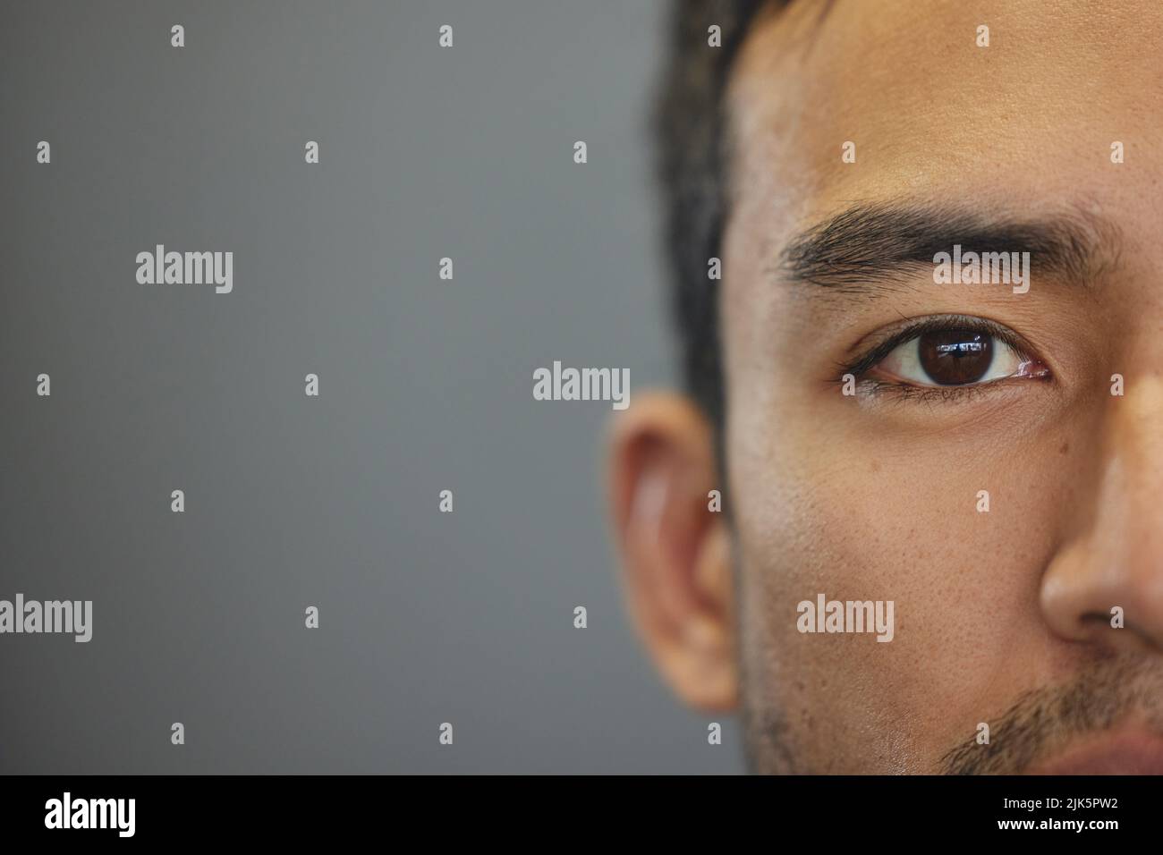 Guardami negli occhi, un bel giovane uomo che si alza su uno sfondo grigio. Foto Stock