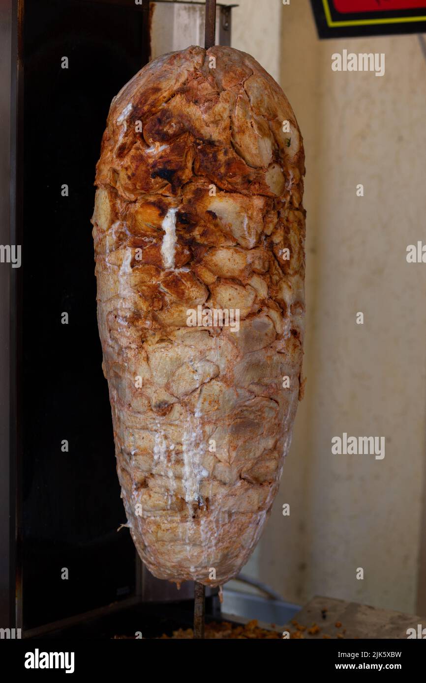 Primo piano di tostatura di carne cruda impilata da utilizzare nella preparazione di gyros tradizionali greci o doner turco durum. Foto Stock
