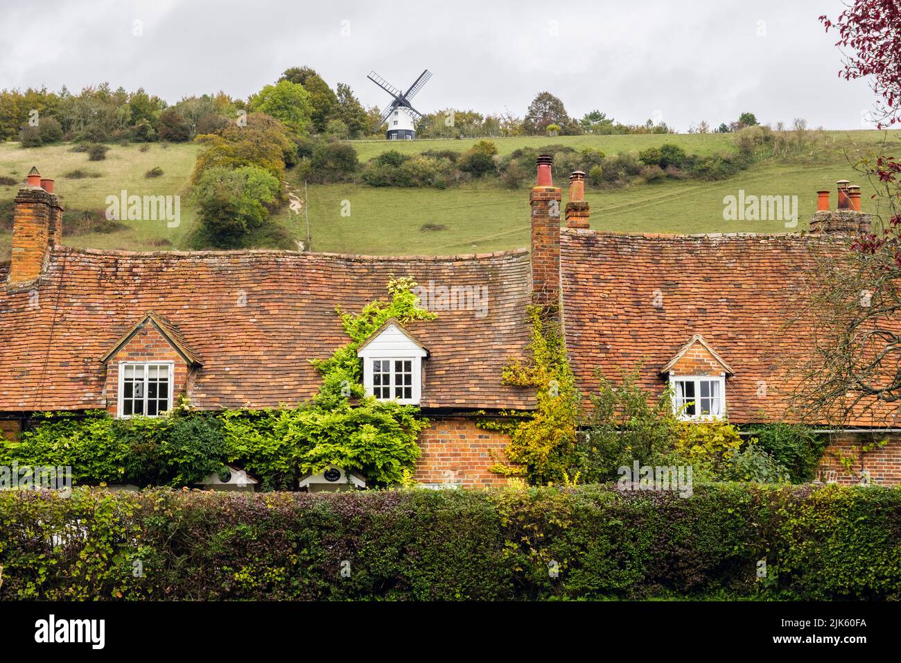 Vecchie case storiche sotto Turville Hill con mulino a vento in villaggio. Turville, Buckinghamshire, Inghilterra, Regno Unito, Gran Bretagna. Un pittoresco villaggio a Chiltern Hills Foto Stock