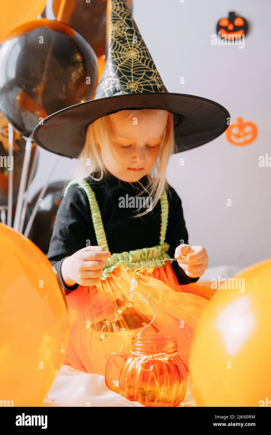 Halloween per bambini - una ragazza in un cappello da strega e un costume  da carnevale con palloncini arancioni e neri a casa. Pronto a festeggiare  Halloween Foto stock - Alamy