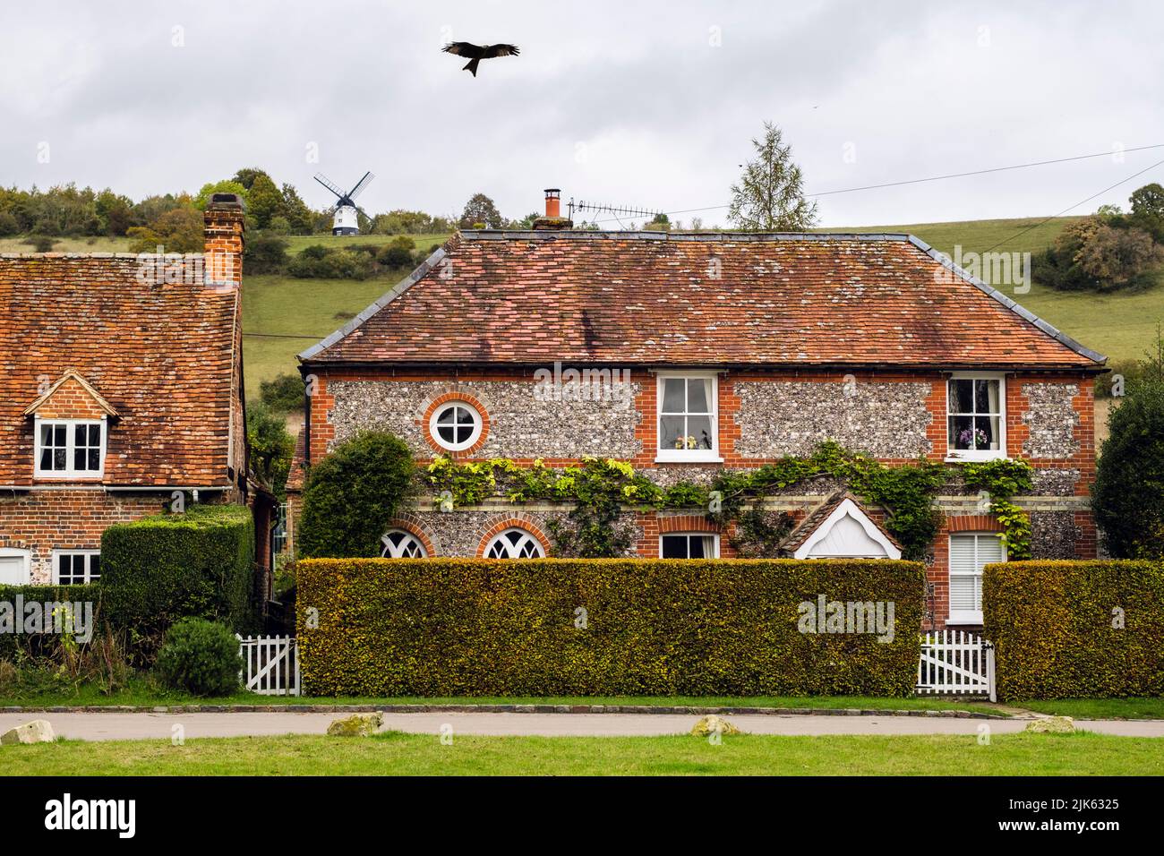 Un aquilone rosso si aggira su vecchi cottage in pietra di pietra sotto Turville Hill con mulino a vento nel villaggio di Chilterns. Turville, Buckinghamshire, Inghilterra, Regno Unito, Gran Bretagna Foto Stock