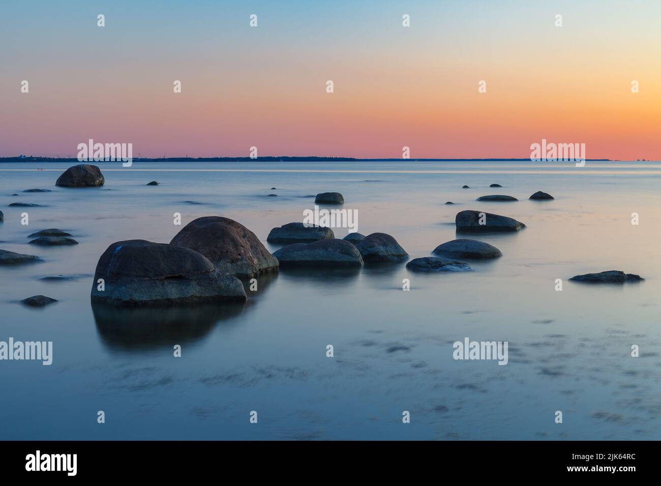 Riva rocciosa con pietre che affondano nell'acqua di mare. Tramonto, esposizione lunga. Mar Baltico Foto Stock