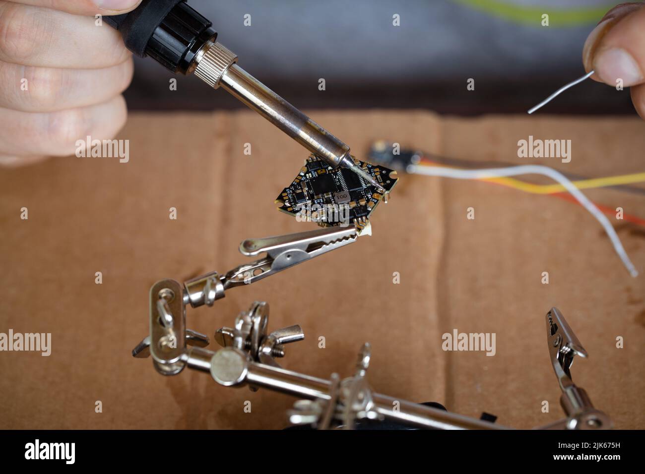 La mano che tiene lo stagno, un saldatore saldano il chip in posizione. Un uomo salda un filo ad un microcircuito Foto Stock