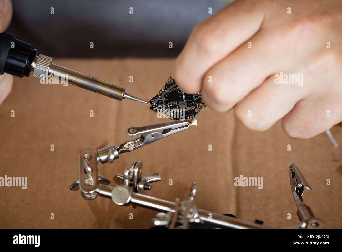 La mano che tiene lo stagno, un saldatore saldano il chip in posizione. Un uomo salda un filo ad un microcircuito Foto Stock