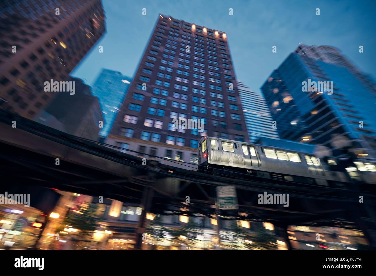 Treno sopraelevato a Chicago in movimento sfocato contro i grattacieli nel centro di notte. Foto Stock