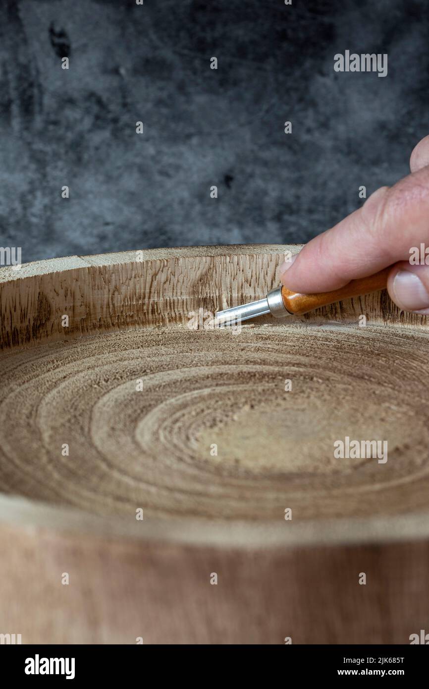 Uomo che intagliano un tronco di legno in una ciotola o in un piatto, con uno scalpello smussato. Su sfondo di pietra scura Foto Stock