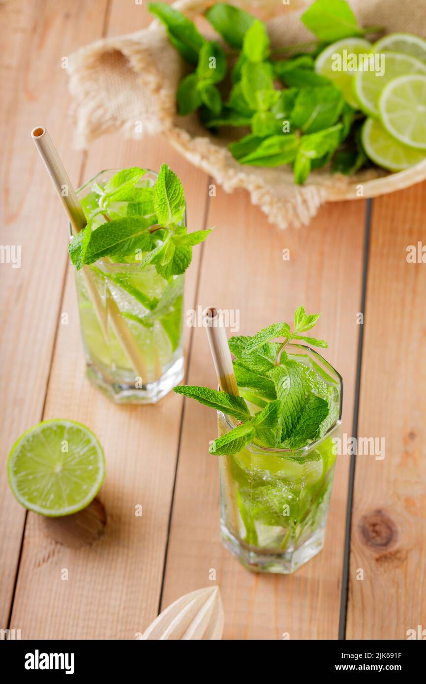 Mojito cocktail e ingredienti su tavole di legno. Due bicchieri di mojito con menta e lime. Drink estivo con cannuccia di bambù Foto Stock