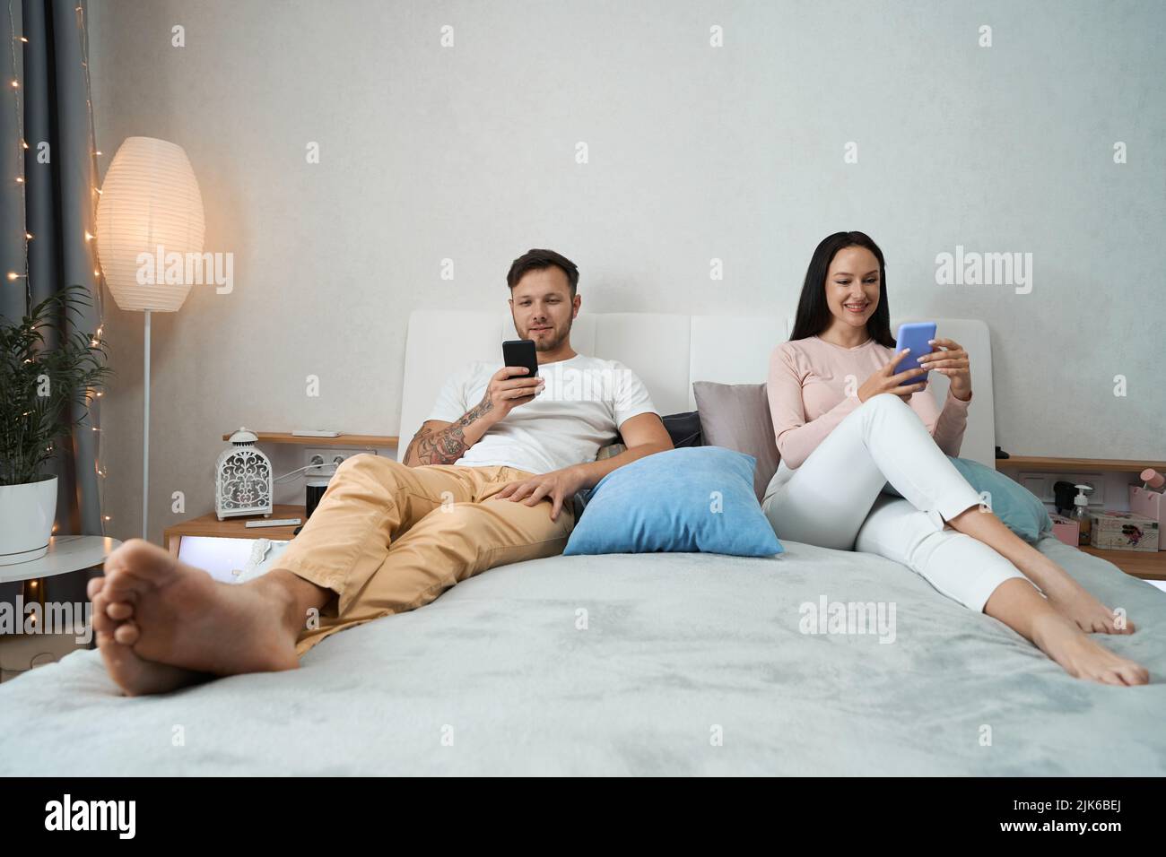 La giovane coppia si siede comodamente tra i cuscini con smartphone Foto Stock