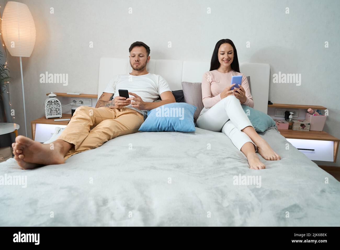 L'uomo e la donna sono seduti con i loro telefoni a letto. Foto Stock