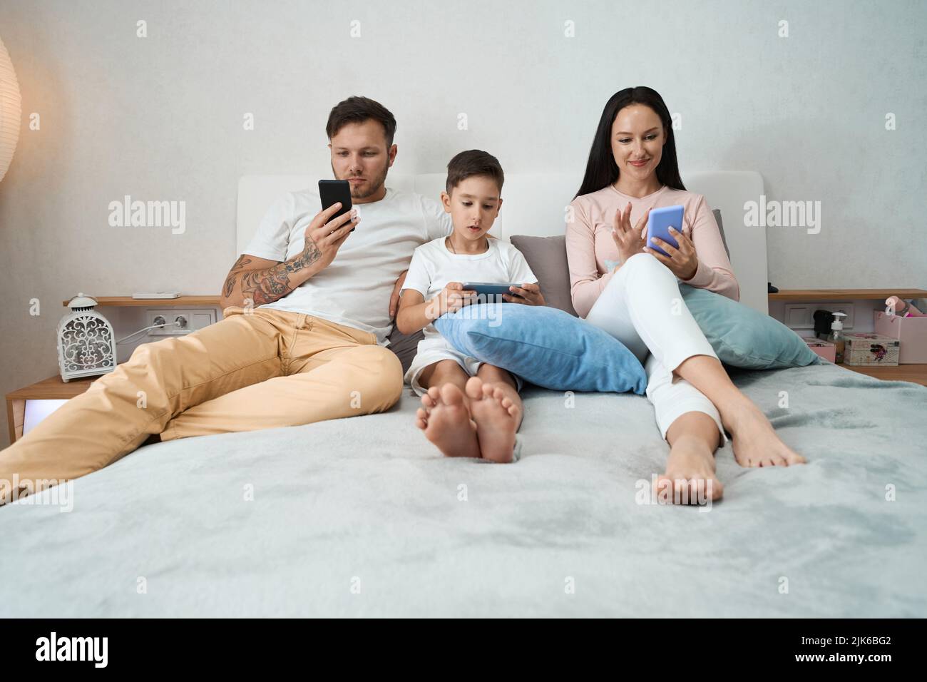 Papà, mamma e figlio sedettero sul letto con gli smartphone Foto Stock