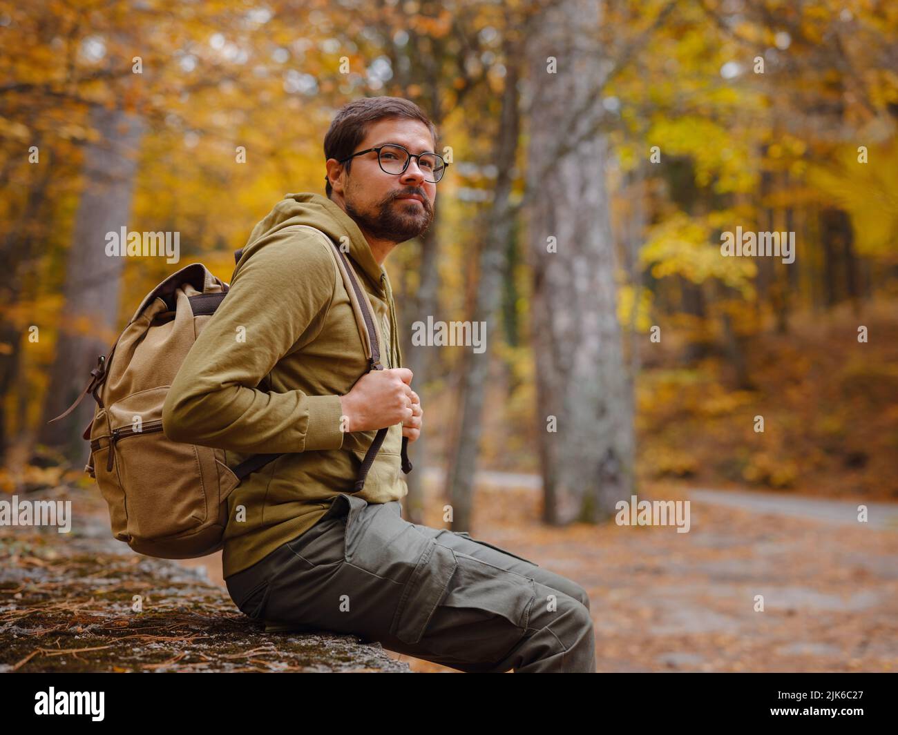 Giovane uomo bello in posa nella foresta d'autunno. Giovane hipster ragazzo con zaino , viaggiatore in piedi in legno, Escursionismo, Foresta, viaggio, attivo sano stile di vita, avventura, concetto di vacanza. Foto Stock