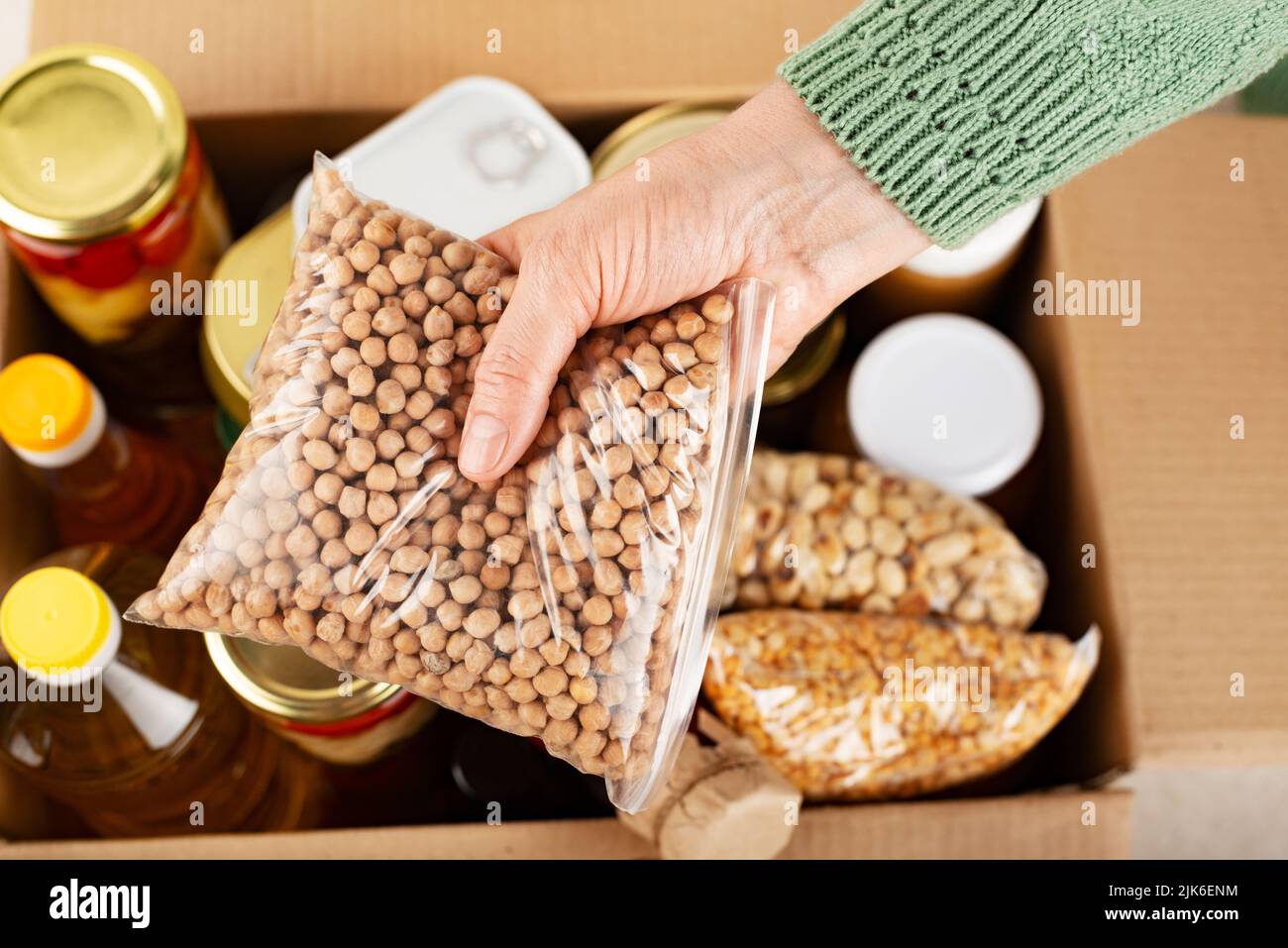 Contenitore in plastica con ceci in mano femmina sullo sfondo della scatola per alimenti di emergenza Foto Stock