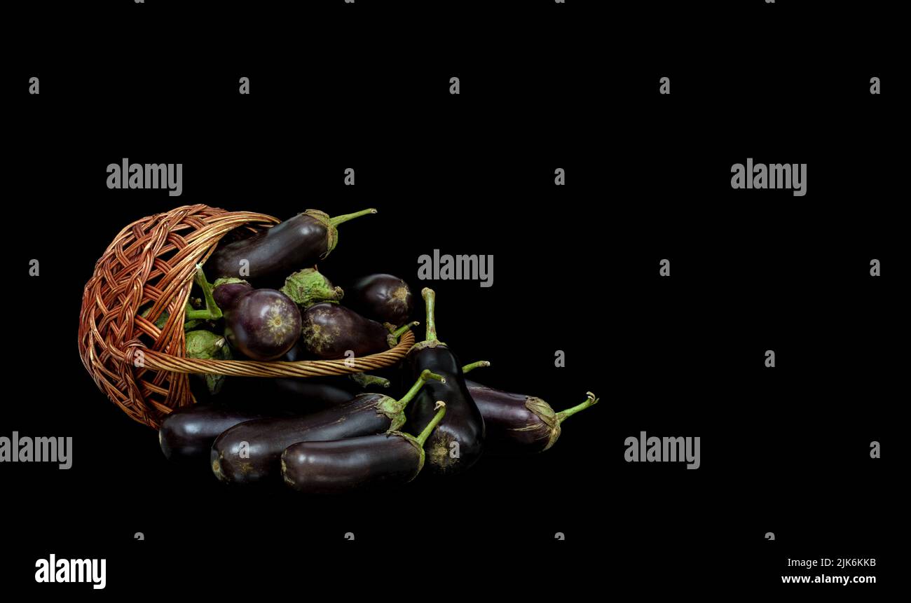 Immagine di un cesto rovesciato con raccolta di melanzane su sfondo nero Foto Stock