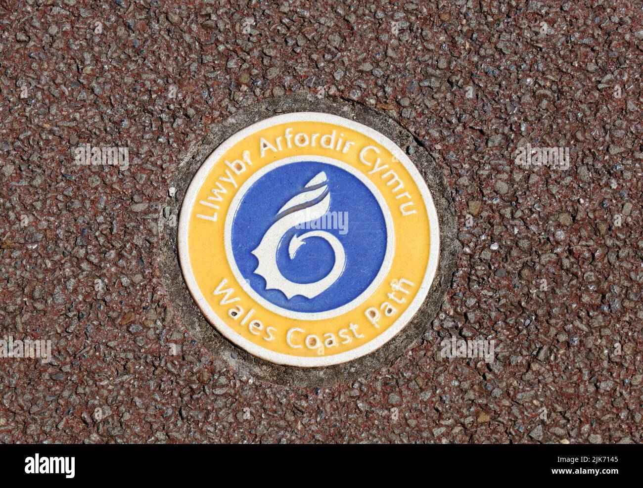 Wales Coast Path piccola placca rotonda immersa in tarmac marrone, sbarramento Cardiff. Scene di Cardiff, luglio 2022. Estate Foto Stock