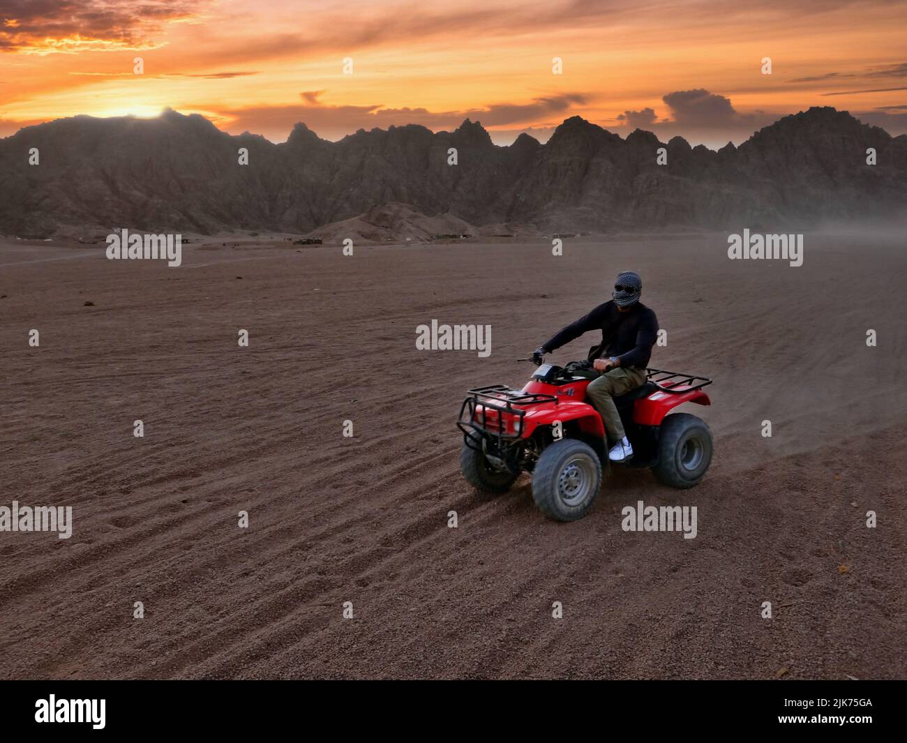 Un uomo irriconoscibile in quad rosso nel deserto egiziano di Sharm el-Sheikh al tramonto Foto Stock