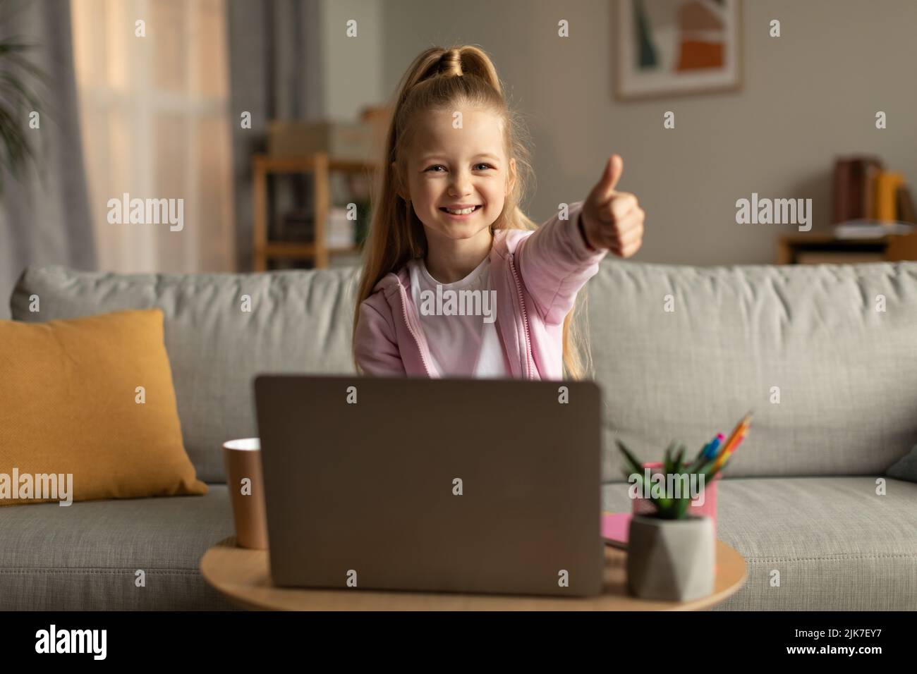 Studentessa che utilizza il notebook gesturando i thumbs in alto approvando l'e-learning a casa Foto Stock