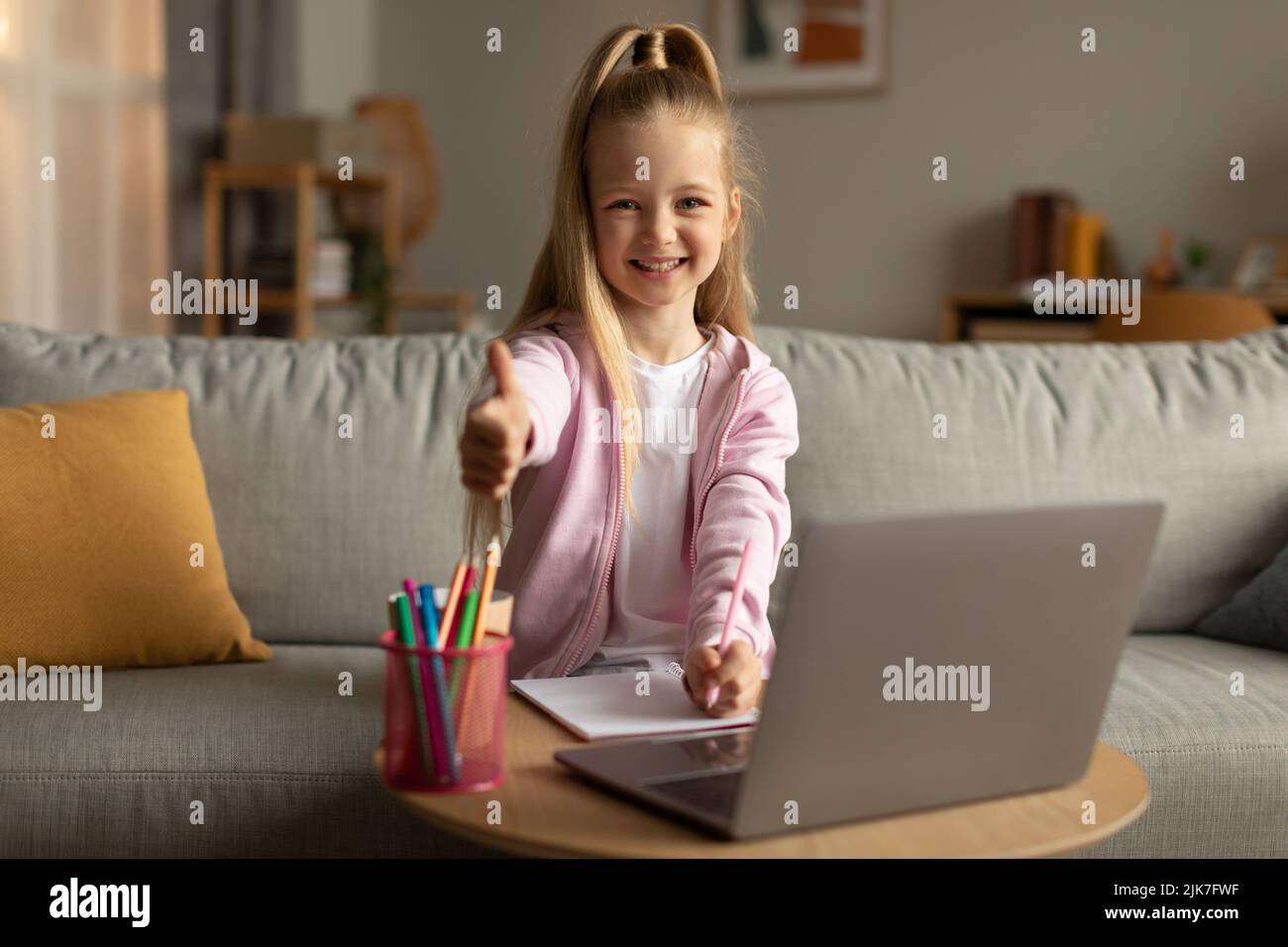 Happy School Kid Girl gesturing Thumbs Up utilizzando notebook Indoor Foto Stock